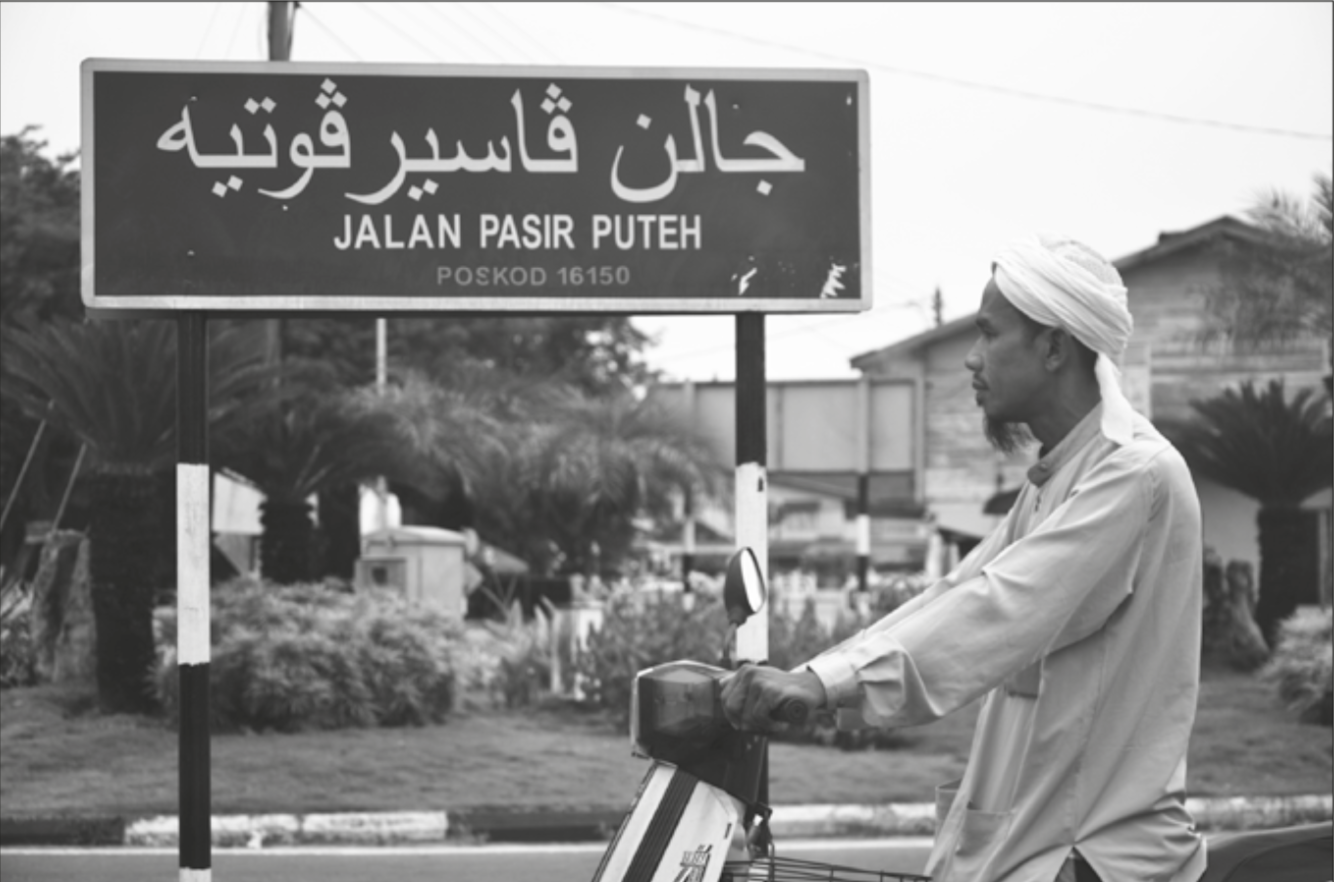 Un panneau indiquant le nom d’une rue en Indonésie en alphabet adjami et en alphabet latin. 